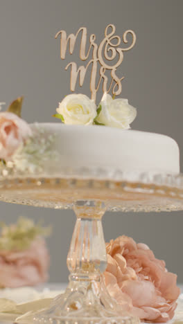 Vertical-Video-Close-Up-Of-Wedding-Cake-On-Stand-Against-Grey-Studio-Background-At-Wedding-Reception-1